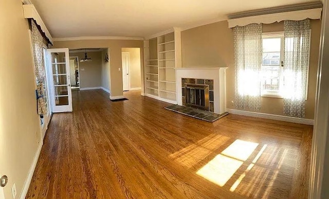 unfurnished living room with a fireplace, hardwood / wood-style flooring, ornamental molding, built in shelves, and french doors