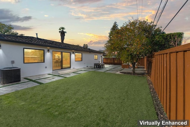 back house at dusk with a patio area, a yard, and central AC