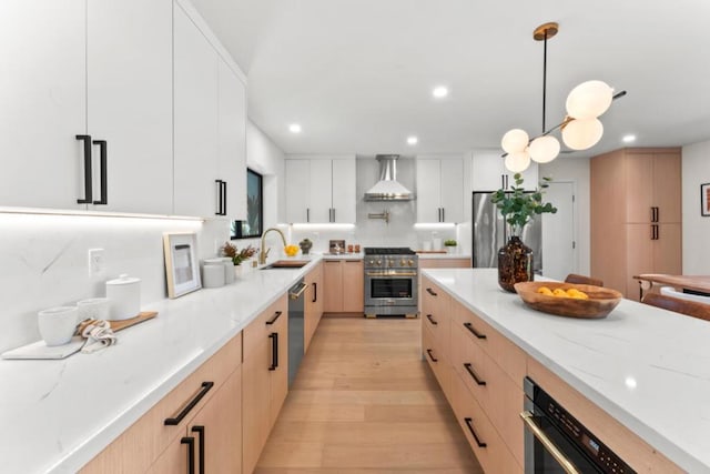 kitchen featuring white cabinets, decorative light fixtures, light hardwood / wood-style flooring, stainless steel appliances, and wall chimney exhaust hood