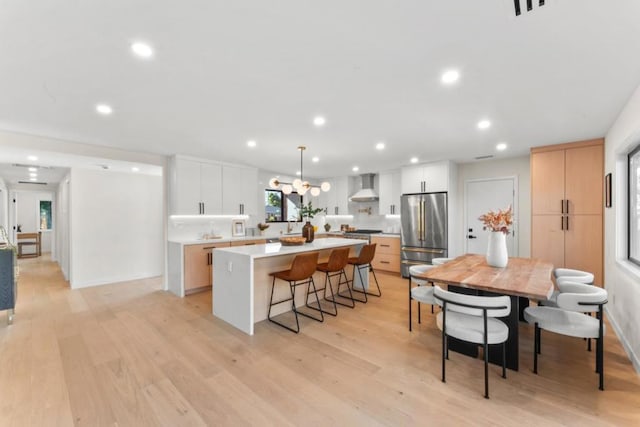 kitchen featuring white cabinets, high quality fridge, hanging light fixtures, and wall chimney exhaust hood