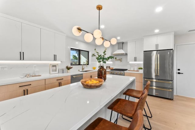 kitchen featuring white cabinets, appliances with stainless steel finishes, wall chimney exhaust hood, decorative light fixtures, and sink