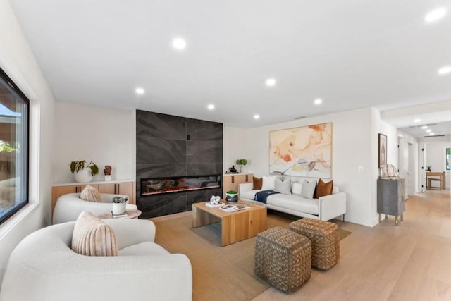 living room featuring plenty of natural light, a tiled fireplace, and light wood-type flooring