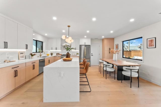 kitchen featuring a center island, white cabinetry, stainless steel appliances, sink, and hanging light fixtures