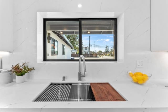 room details with white cabinets, backsplash, light stone countertops, and sink