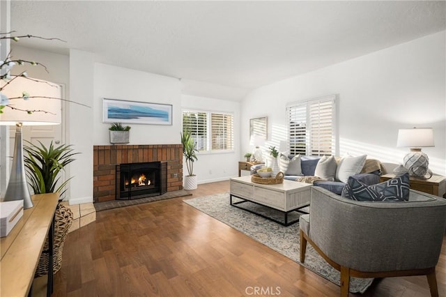 living room featuring vaulted ceiling, a brick fireplace, and hardwood / wood-style floors