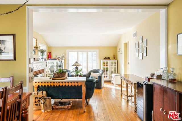 living room featuring light hardwood / wood-style flooring, beverage cooler, and vaulted ceiling