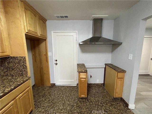 kitchen featuring wall chimney range hood, dark stone counters, and tasteful backsplash