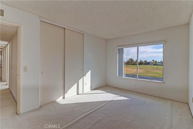 unfurnished bedroom with light carpet, a textured ceiling, and a closet