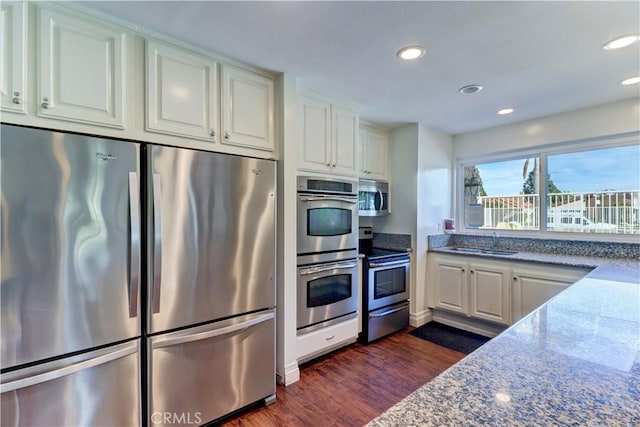 kitchen with white cabinets, sink, dark wood-type flooring, stainless steel appliances, and stone countertops