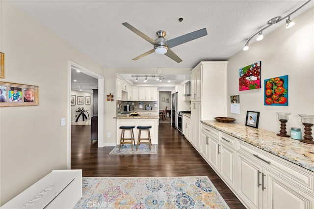 kitchen with appliances with stainless steel finishes, white cabinetry, light stone counters, a kitchen bar, and decorative backsplash