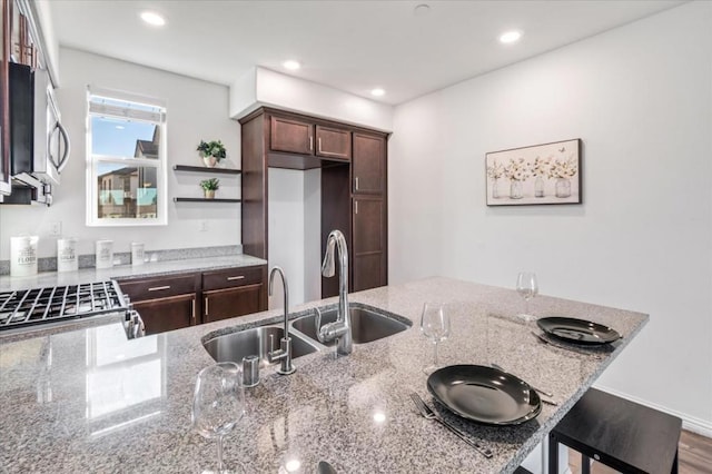 kitchen with light stone counters, sink, and dark brown cabinets