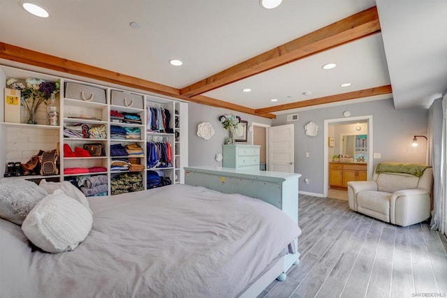 bedroom featuring beam ceiling, a closet, ensuite bath, and light wood-type flooring