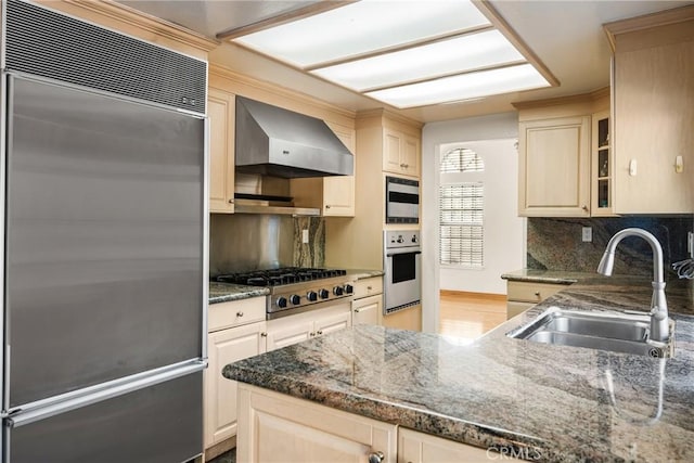 kitchen featuring dark stone counters, sink, backsplash, stainless steel appliances, and wall chimney exhaust hood