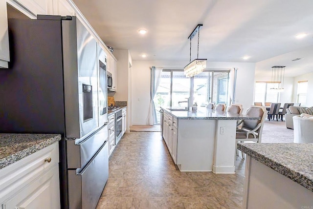 kitchen featuring stainless steel appliances, a breakfast bar, white cabinets, and decorative light fixtures