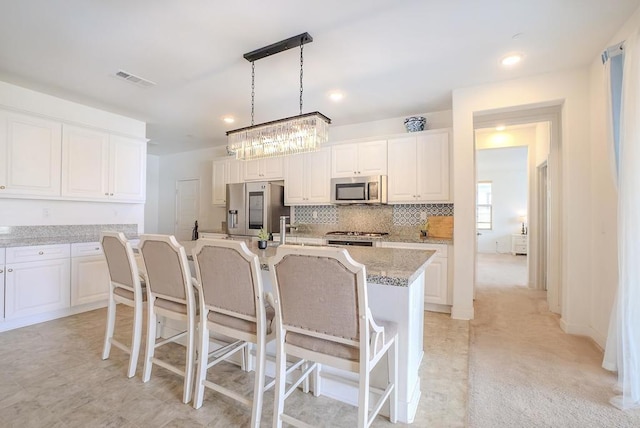 kitchen featuring light stone counters, decorative light fixtures, a center island with sink, appliances with stainless steel finishes, and white cabinets