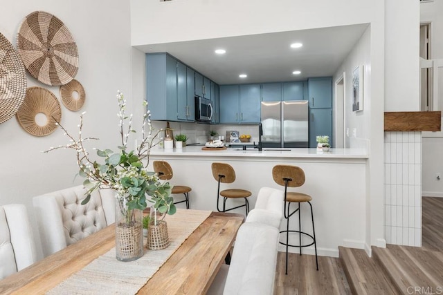 kitchen with kitchen peninsula, appliances with stainless steel finishes, blue cabinetry, backsplash, and hardwood / wood-style floors