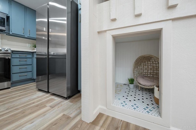 kitchen featuring blue cabinets, light hardwood / wood-style flooring, and appliances with stainless steel finishes