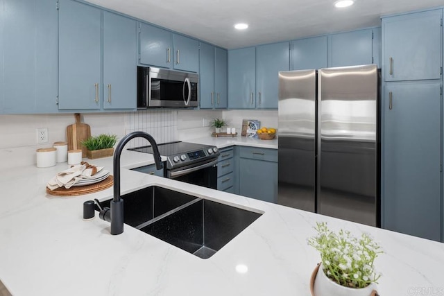 kitchen featuring light stone countertops, appliances with stainless steel finishes, decorative backsplash, blue cabinetry, and sink