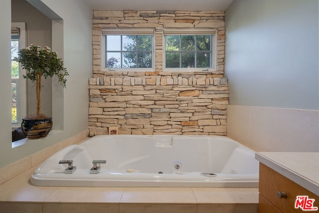 bathroom featuring a healthy amount of sunlight, tiled bath, and vanity