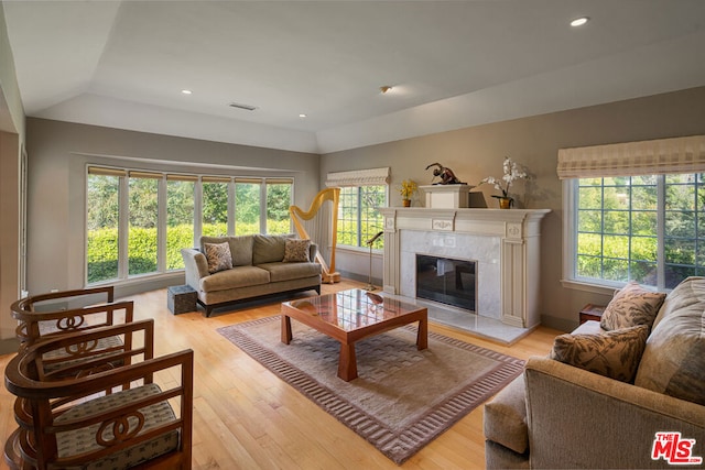 living room featuring light hardwood / wood-style floors, a high end fireplace, and vaulted ceiling