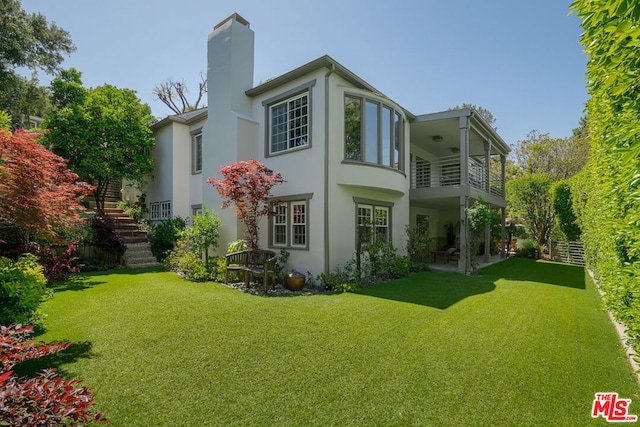 rear view of property with a balcony, a patio area, a lawn, and ceiling fan