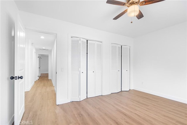 unfurnished bedroom with ceiling fan, light hardwood / wood-style flooring, and two closets