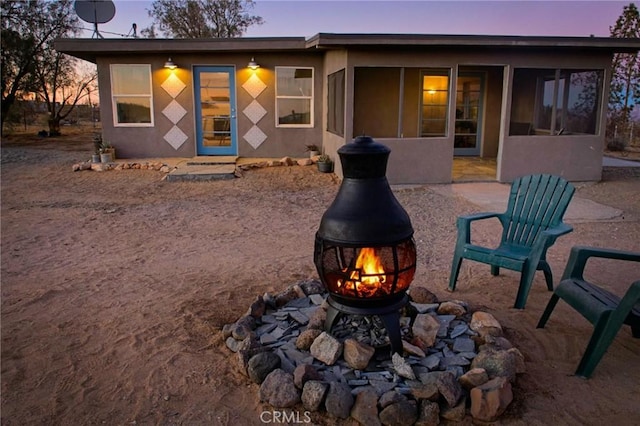 back house at dusk with an outdoor fire pit and a sunroom