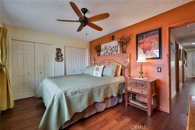 bedroom with ceiling fan, a textured ceiling, dark wood-type flooring, and multiple closets