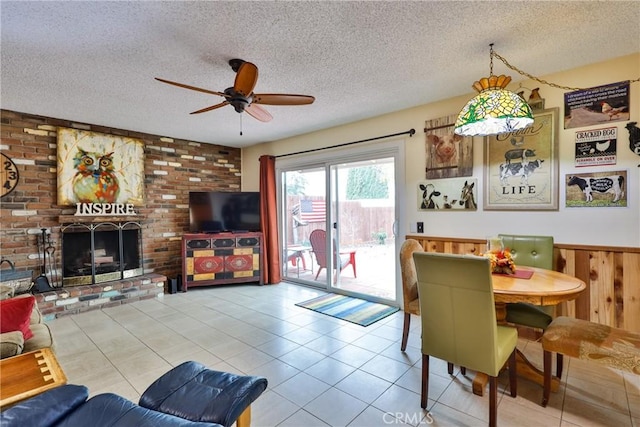 dining area with wood walls, a textured ceiling, light tile patterned floors, ceiling fan, and a fireplace