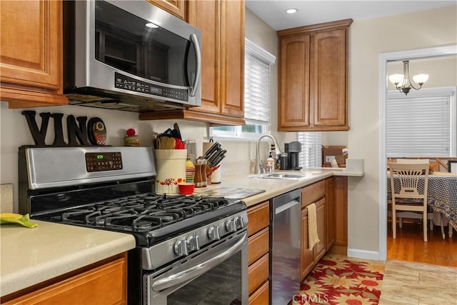 kitchen with appliances with stainless steel finishes, sink, a notable chandelier, and light hardwood / wood-style flooring