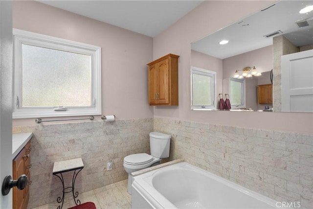 bathroom with toilet, tile walls, vanity, a bathtub, and tile patterned flooring