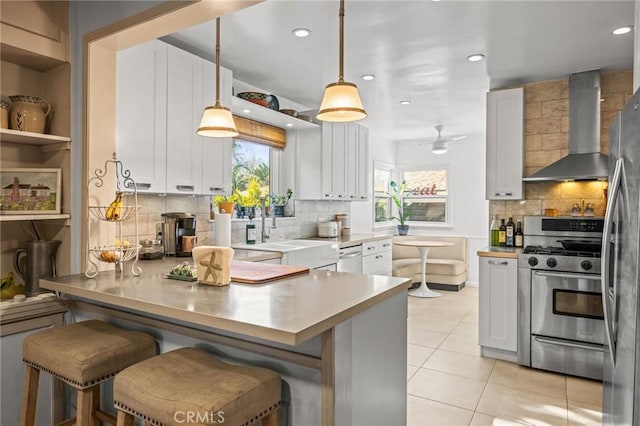 kitchen featuring wall chimney range hood, white cabinetry, appliances with stainless steel finishes, and a breakfast bar