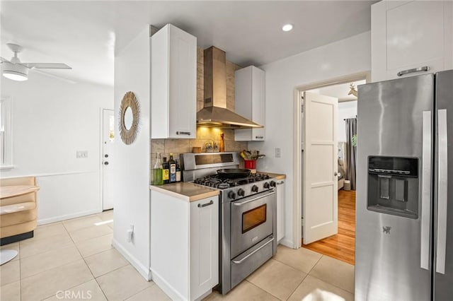 kitchen featuring appliances with stainless steel finishes, white cabinetry, light tile patterned floors, wall chimney range hood, and decorative backsplash