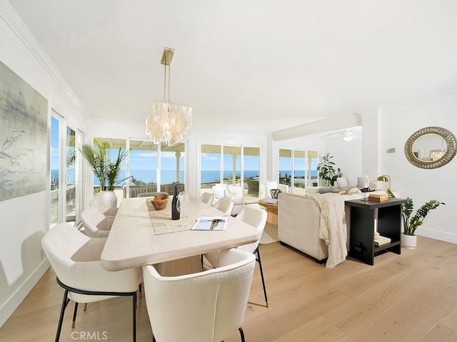 dining space with ornamental molding, a water view, a chandelier, and light hardwood / wood-style flooring