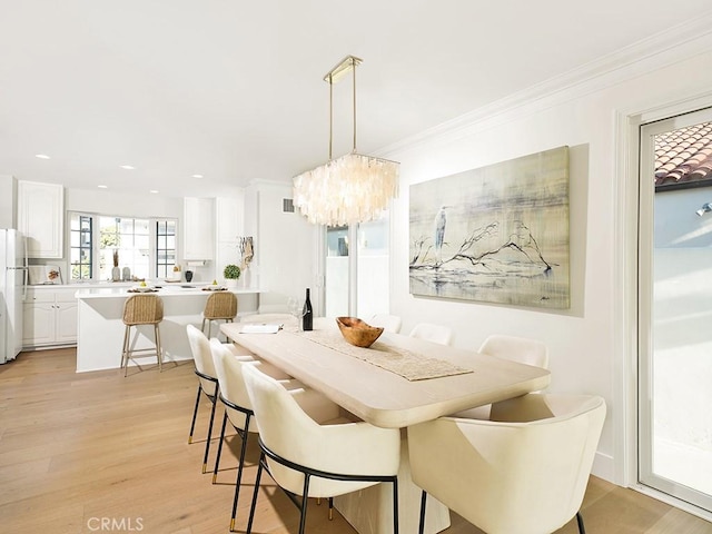 dining space with an inviting chandelier, ornamental molding, and light wood-type flooring