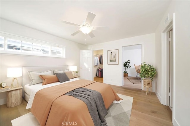 bedroom with a spacious closet, a closet, ceiling fan, and light wood-type flooring