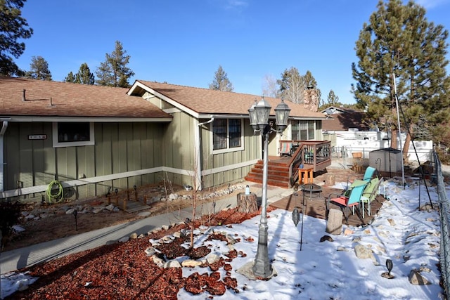 snow covered back of property featuring an outdoor fire pit and a storage unit