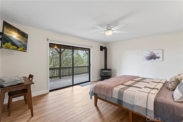 bedroom featuring light hardwood / wood-style floors, ceiling fan, access to outside, and a wood stove