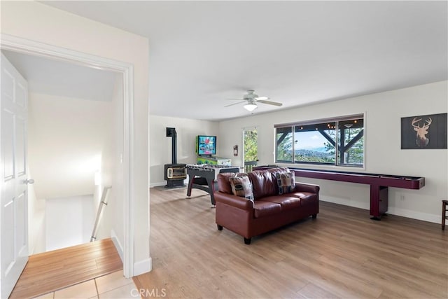 living room with ceiling fan, a wood stove, and light wood-type flooring