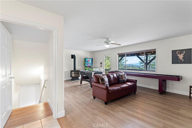 living room with ceiling fan, a wood stove, and light hardwood / wood-style floors