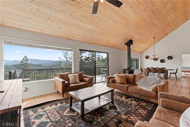 living room with a mountain view, a wood stove, ceiling fan, wooden ceiling, and tile patterned flooring