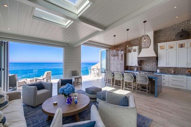 living room with a water view, brick wall, vaulted ceiling with skylight, and light wood-type flooring