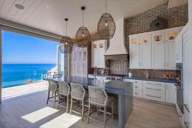 interior space featuring decorative light fixtures, white cabinetry, decorative backsplash, a water view, and light hardwood / wood-style flooring