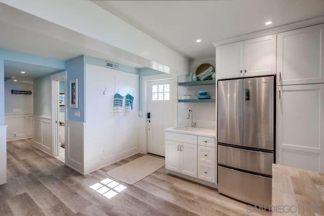 kitchen featuring sink, white cabinets, stainless steel refrigerator, and light wood-type flooring