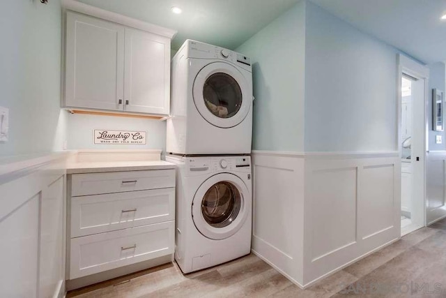 washroom with stacked washer and dryer, cabinets, and light hardwood / wood-style floors