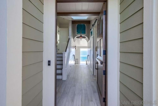 hall featuring wooden walls, a skylight, beam ceiling, and light hardwood / wood-style flooring