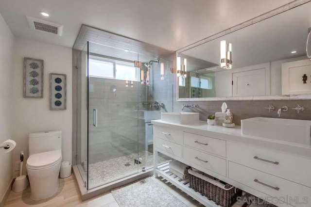 bathroom featuring vanity, toilet, backsplash, and a shower with shower door