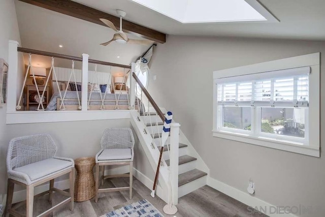 staircase with ceiling fan, wood-type flooring, and lofted ceiling with skylight