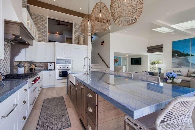 kitchen with pendant lighting, white cabinets, a large island with sink, and appliances with stainless steel finishes