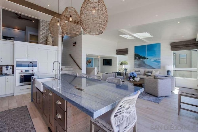 kitchen with sink, white cabinetry, hanging light fixtures, an island with sink, and stainless steel oven